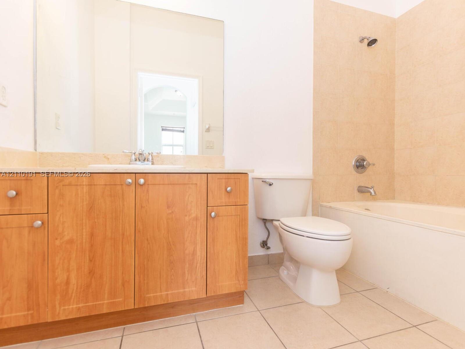 Bathroom featuring wood-finish cabinetry, a neutral stone countertop with an integrated basin, a wall-to-wall vanity mirror, ceramic tile flooring, and a tub-shower combination with tiled surround