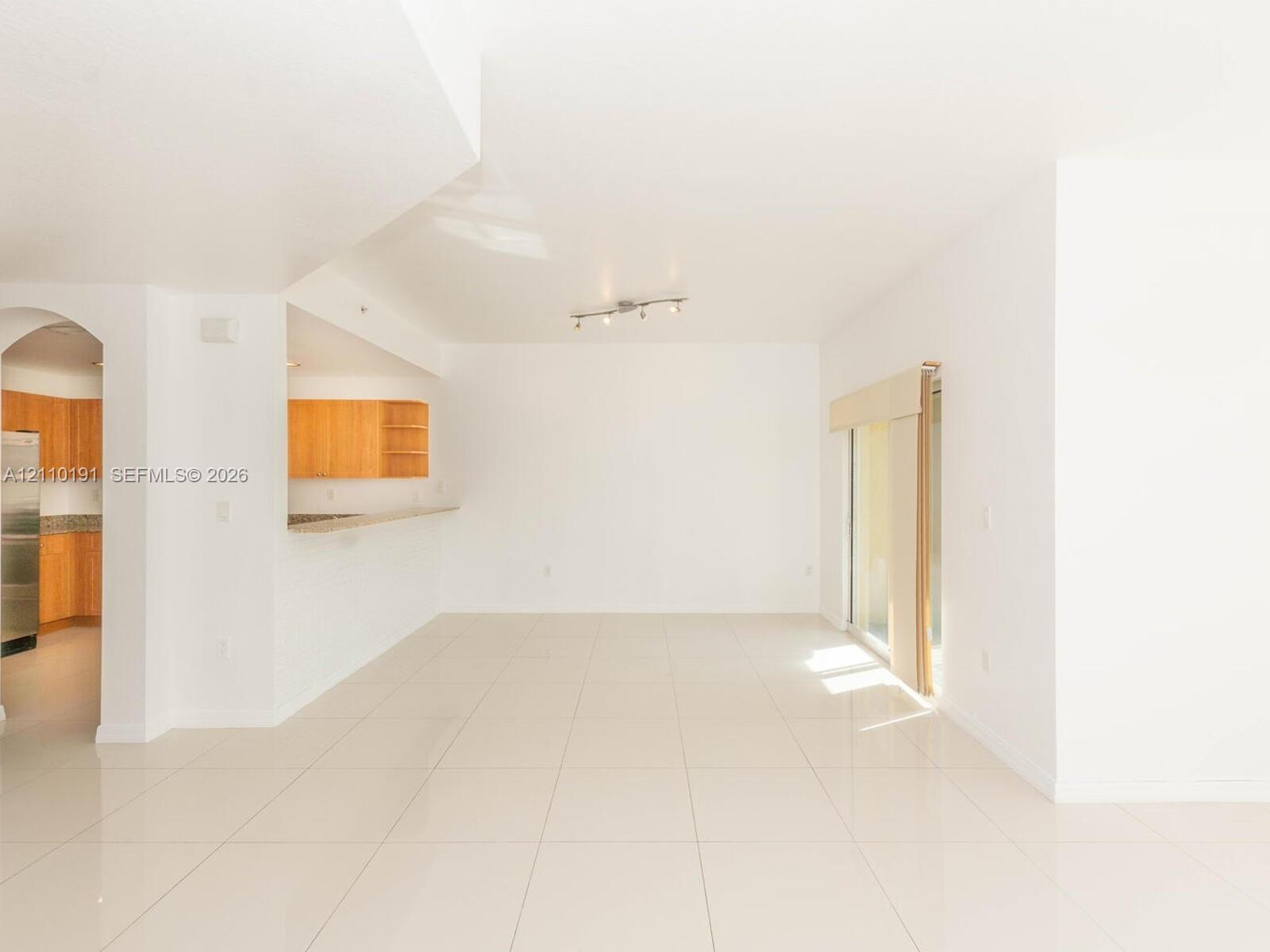 Open-concept interior featuring large-format tile flooring, arched architectural detail, sliding glass doors, and a breakfast bar with wood-toned cabinetry