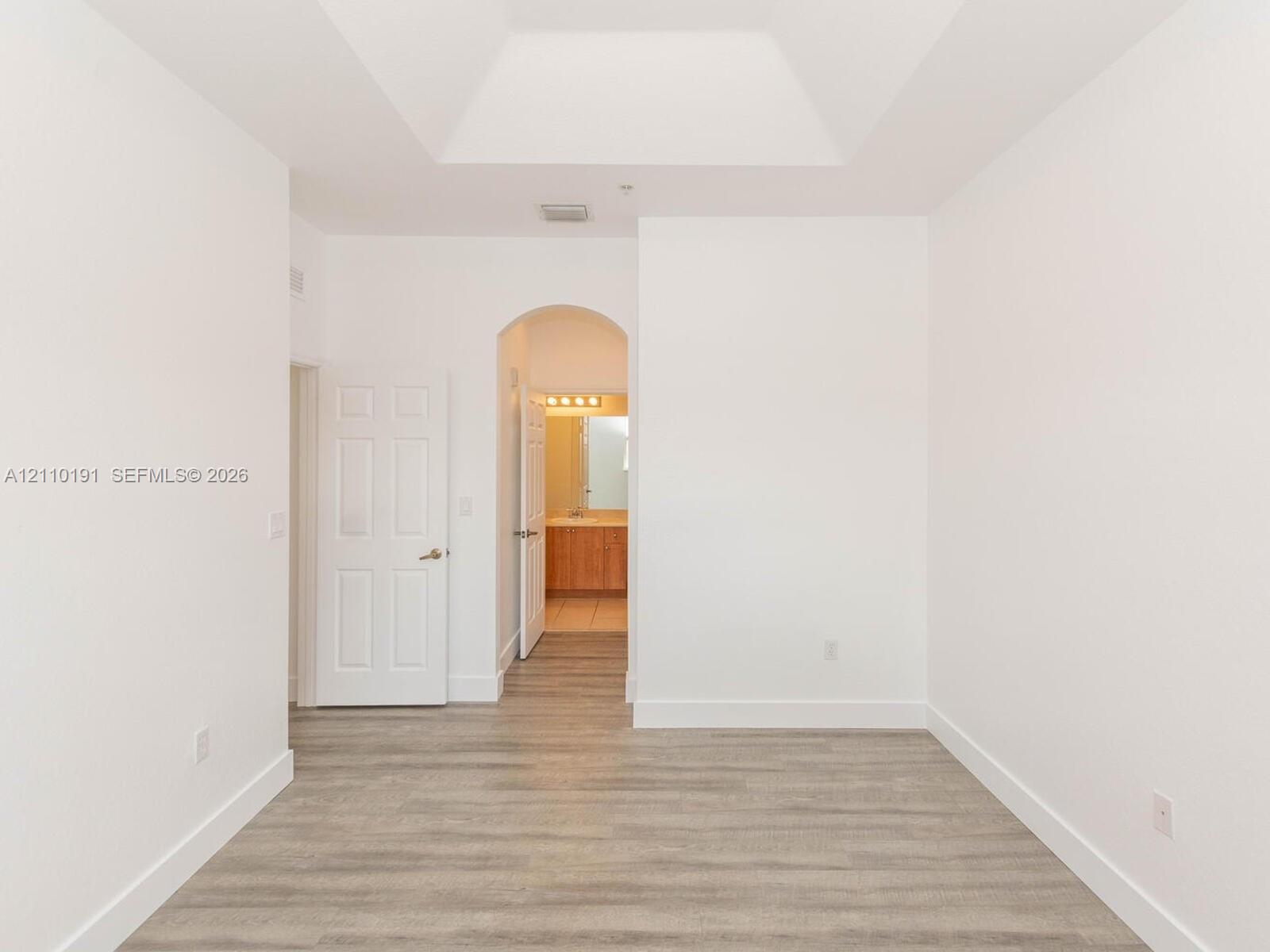 Tray ceiling, wood-finish flooring, and arched architectural detail