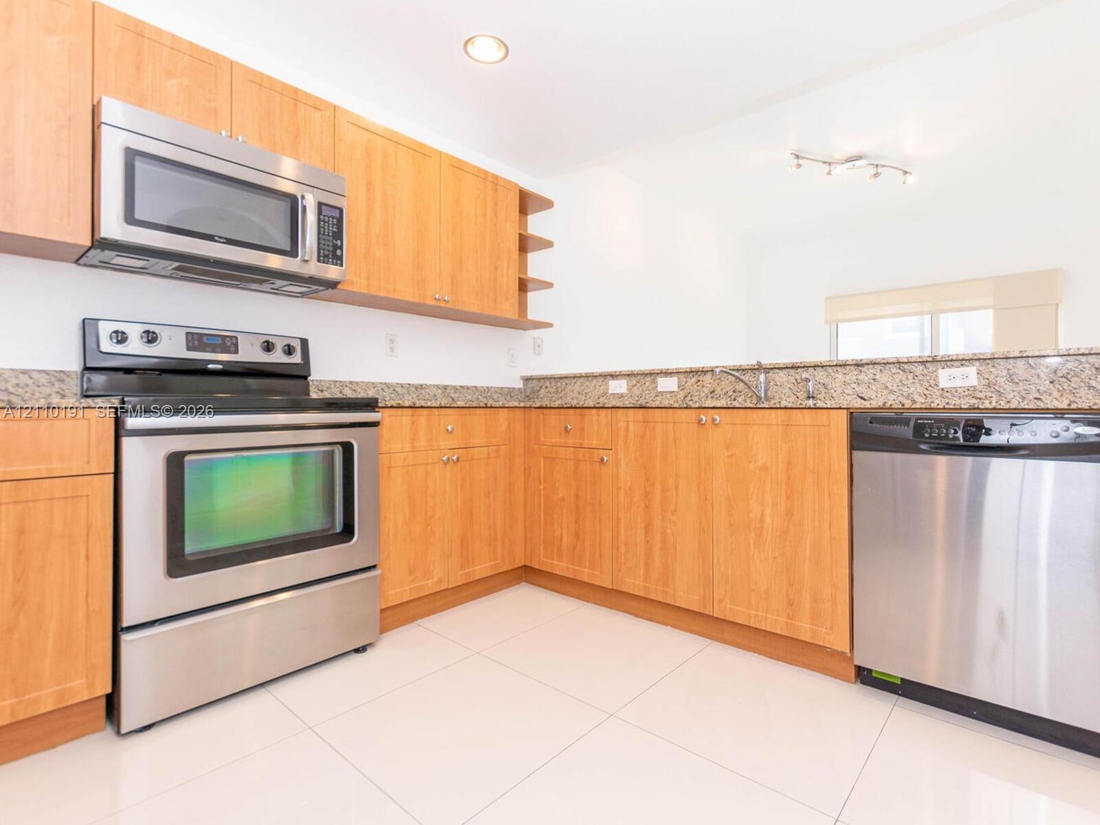Kitchen featuring light wood-finish cabinetry, stone-surface countertops, stainless steel appliances, and tile flooring