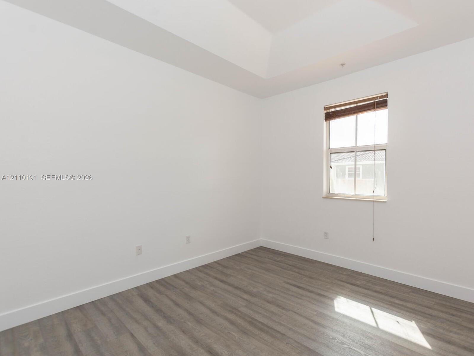 Room featuring a tray ceiling, wood-finish flooring, and a window with integrated blinds