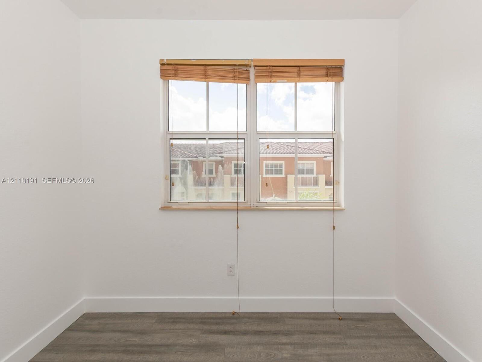 Neutral wall tones paired with gray wood-finish flooring and double-hung window featuring built-in wood-slat blinds