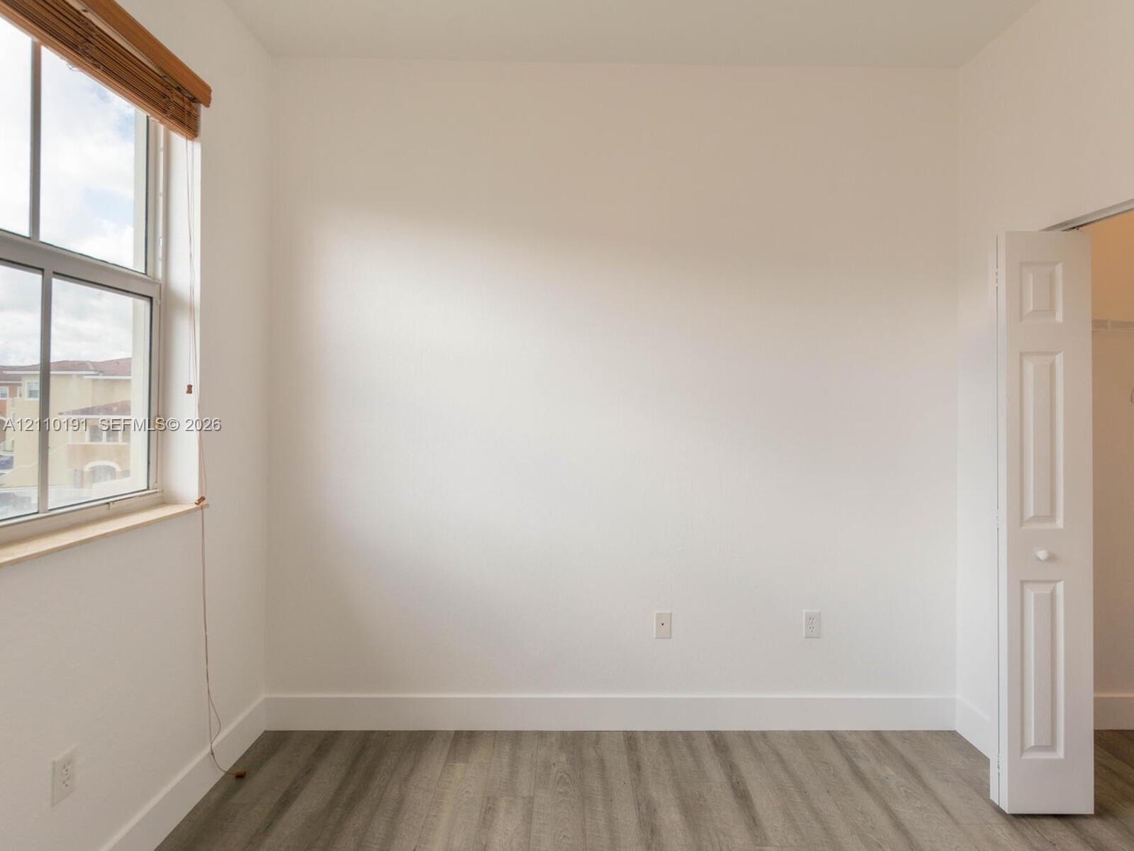 Neutral-toned interior space featuring wood-finish flooring, a multi-pane window with wood-trim blinds, and a paneled bifold closet door