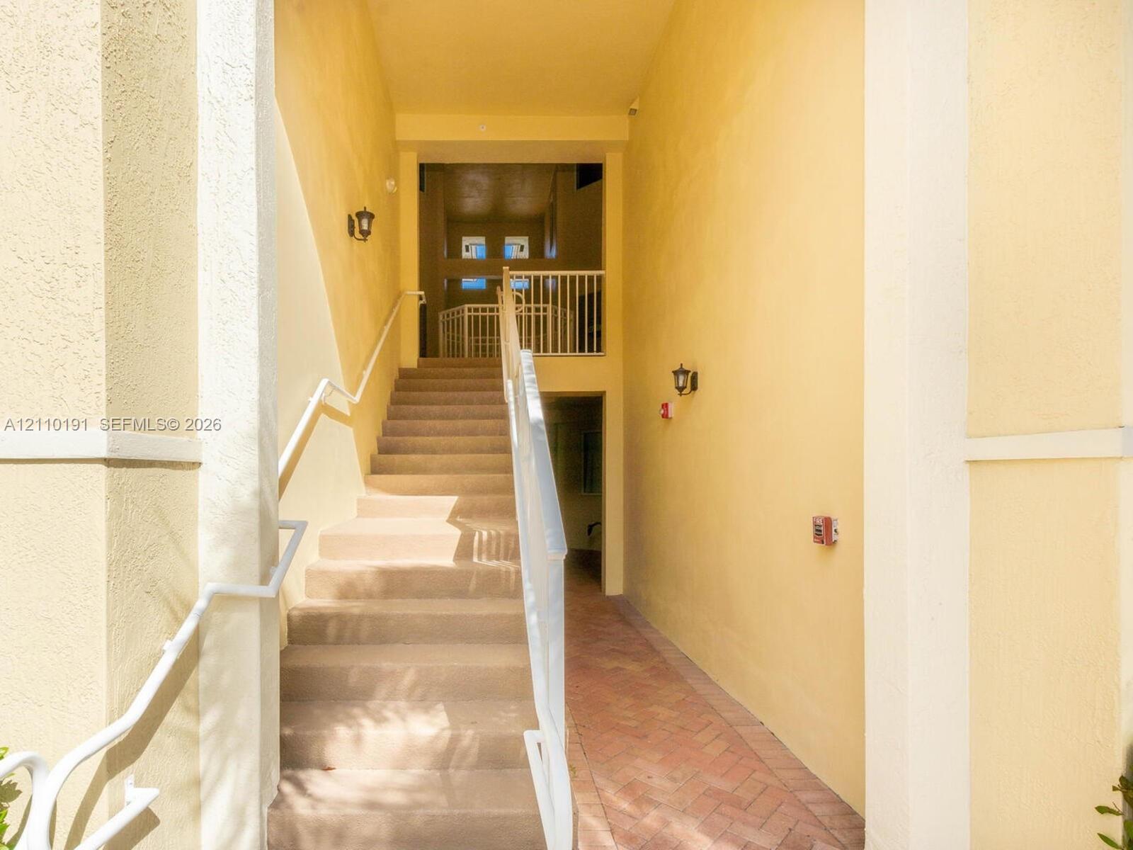 Exterior staircase featuring stucco walls, a herringbone-pattern brick pathway, and white metal railings Exterior staircase featuring stucco walls, a herringbone-pattern brick pathway, and white metal railings