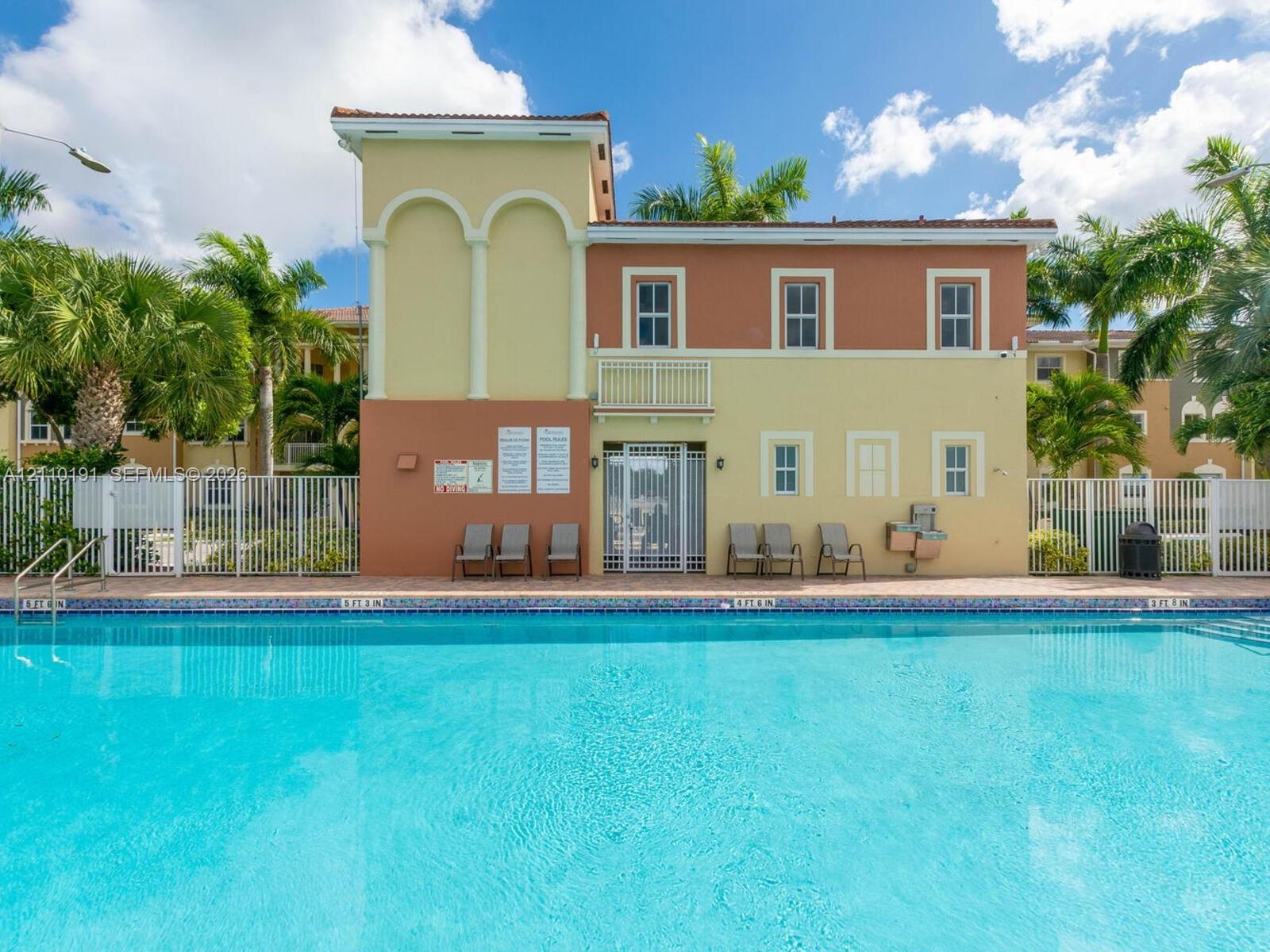 Swimming pool with tile edging, paver pool deck, two-story structure with stucco exterior, arched architectural detailing, and metal perimeter fencing