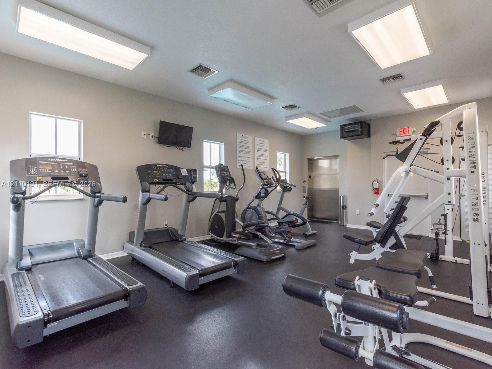 Fitness center featuring rubber flooring, recessed square light fixtures, multiple windows, and a multi-station exercise machine