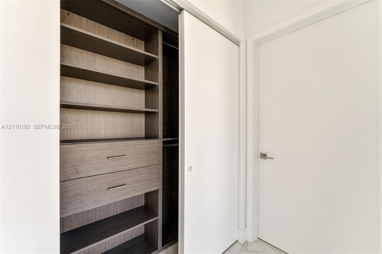 Built-in closet system featuring dark wood-finish shelving, two integrated storage drawers with metal hardware, a hanging rod, and a white sliding door