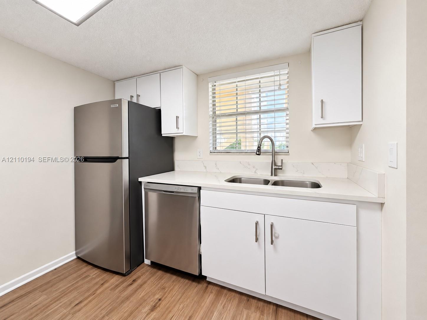 Kitchen featuring stainless steel refrigerator and dishwasher, white cabinetry, light-toned countertop with matching backsplash, and wood-finish flooring