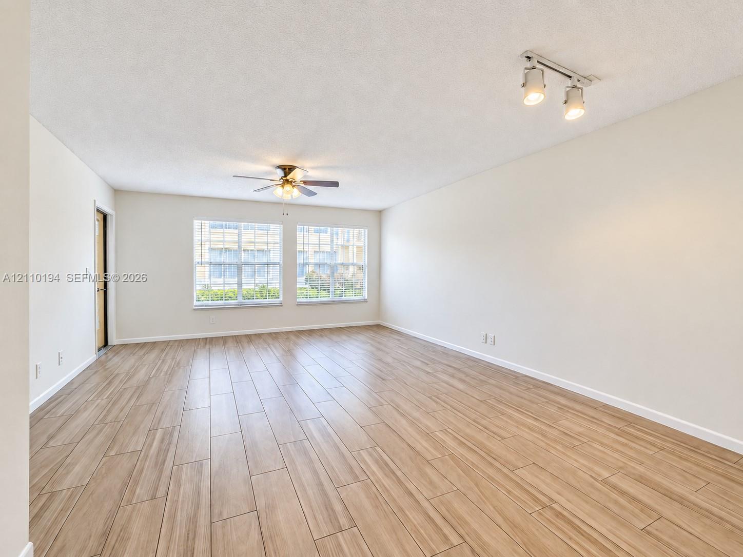 Neutral-toned interior featuring wood-finish tile flooring, dual-pane windows, a ceiling fan with integrated lighting, and a multi-directional track lighting fixture