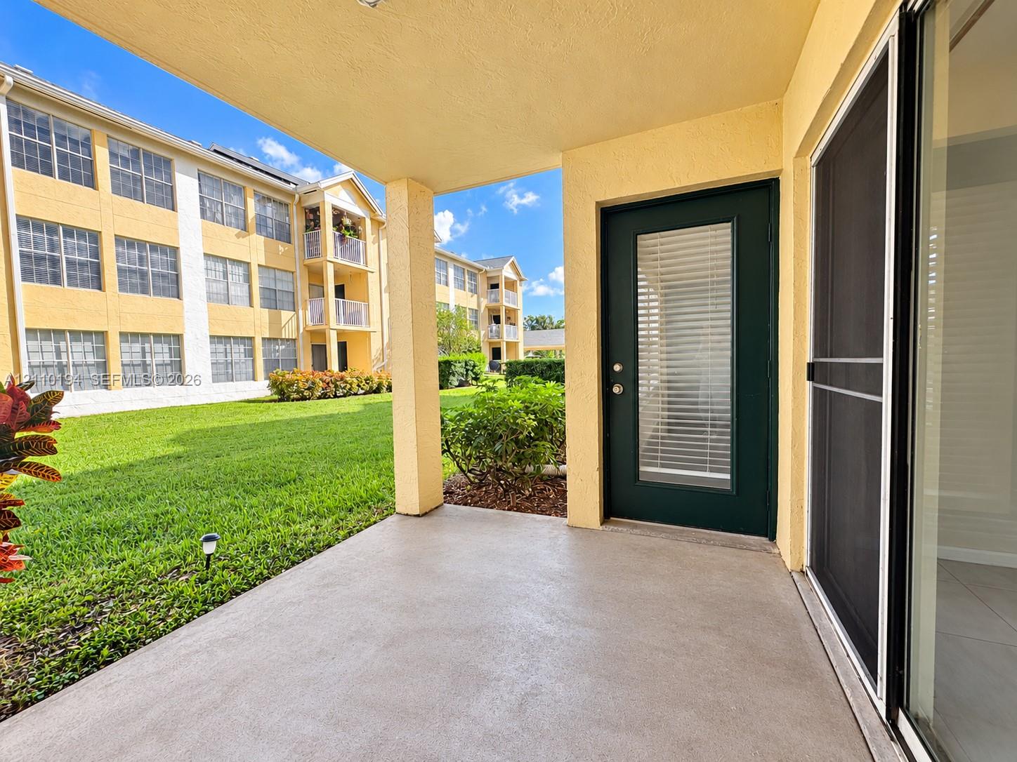 Covered concrete patio featuring a solid-color door with inset window, sliding glass door with mesh screen, and exterior lighting