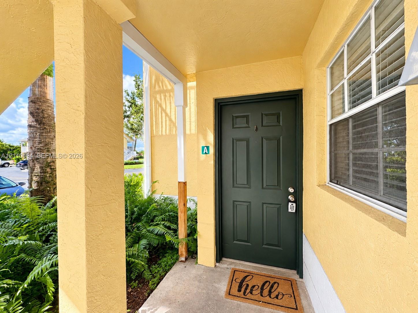 Covered entryway featuring a solid six-panel dark green door, structural column supports, and a single-hung window with a screen