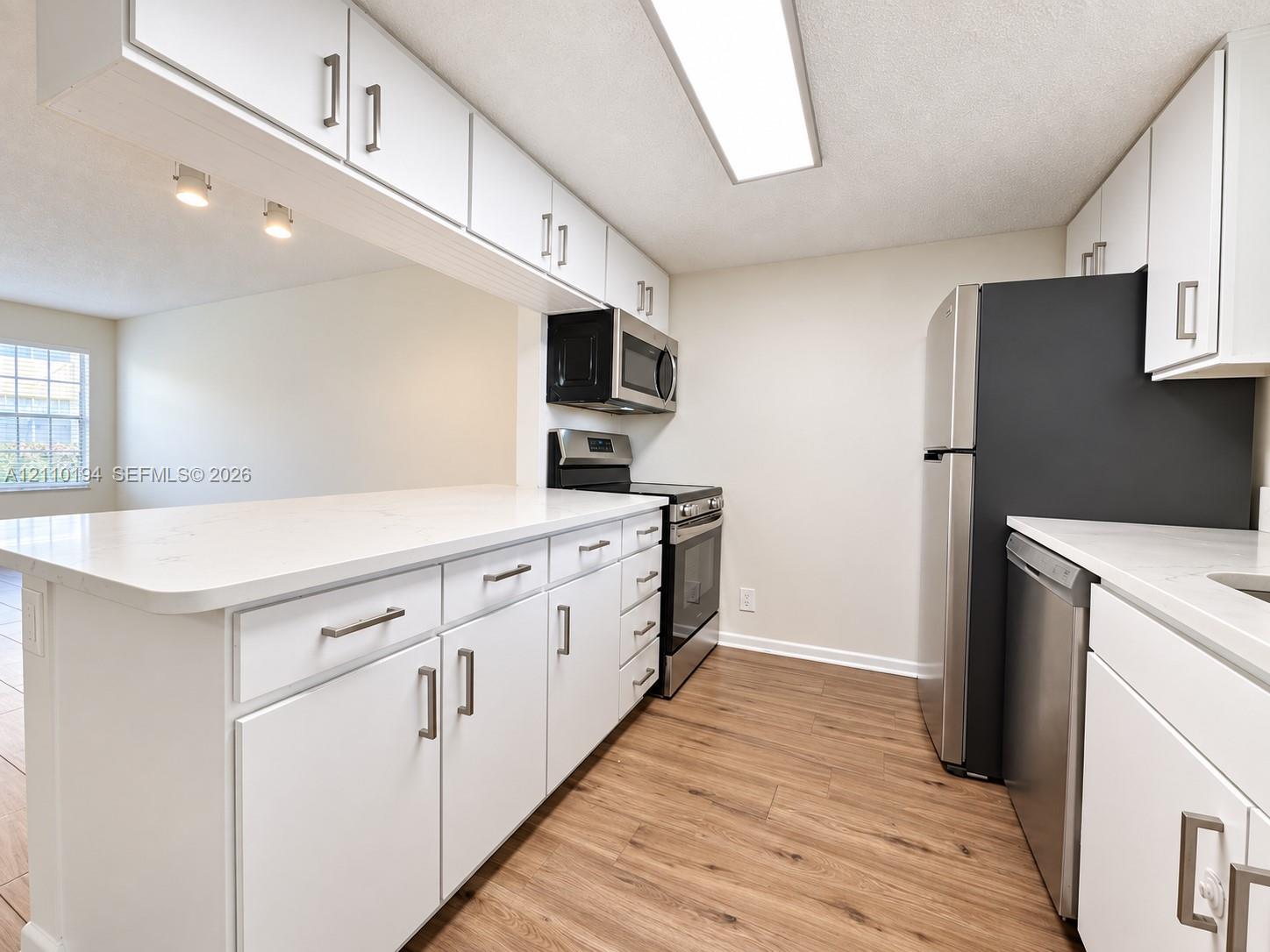 Kitchen featuring white shaker-style cabinetry, solid-surface countertops, wood-finish flooring, and a stainless steel appliance suite