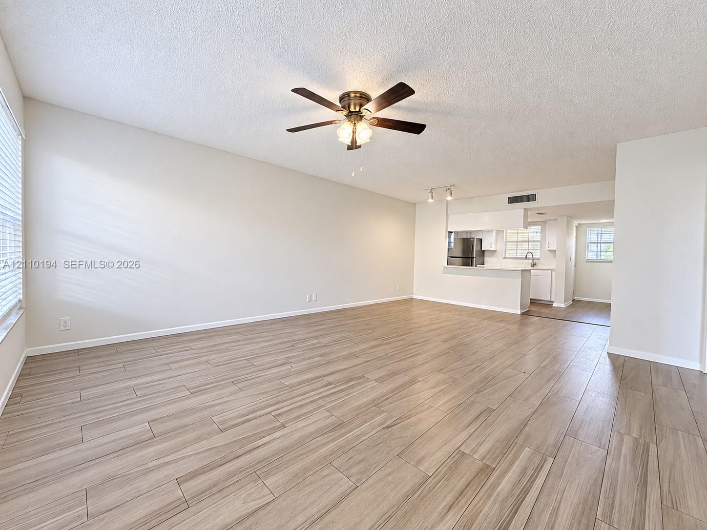 Open-concept interior featuring wood-finish tile flooring, ceiling fan with integrated lighting, and breakfast bar