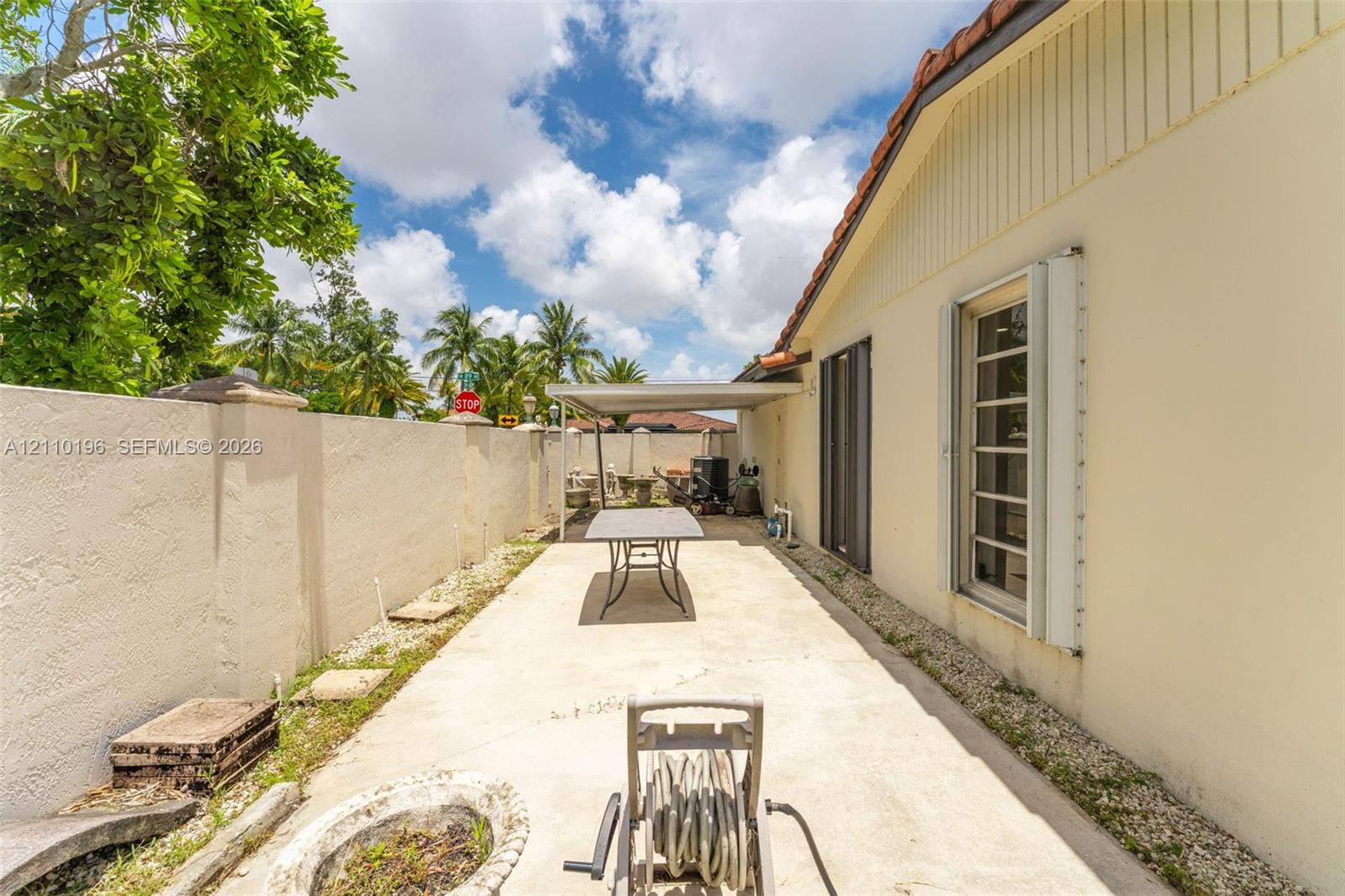 Side patio featuring a concrete surface, enclosed by a solid masonry privacy wall, and partially shaded by a permanent metal awning