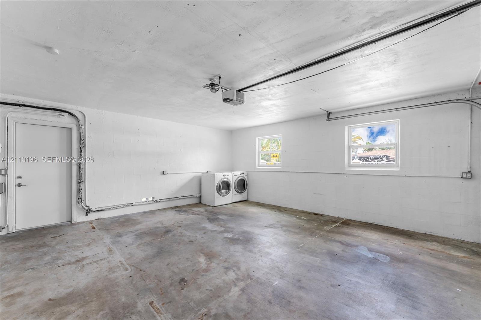 Garage space featuring concrete flooring, painted block walls, two windows, and an exterior access door