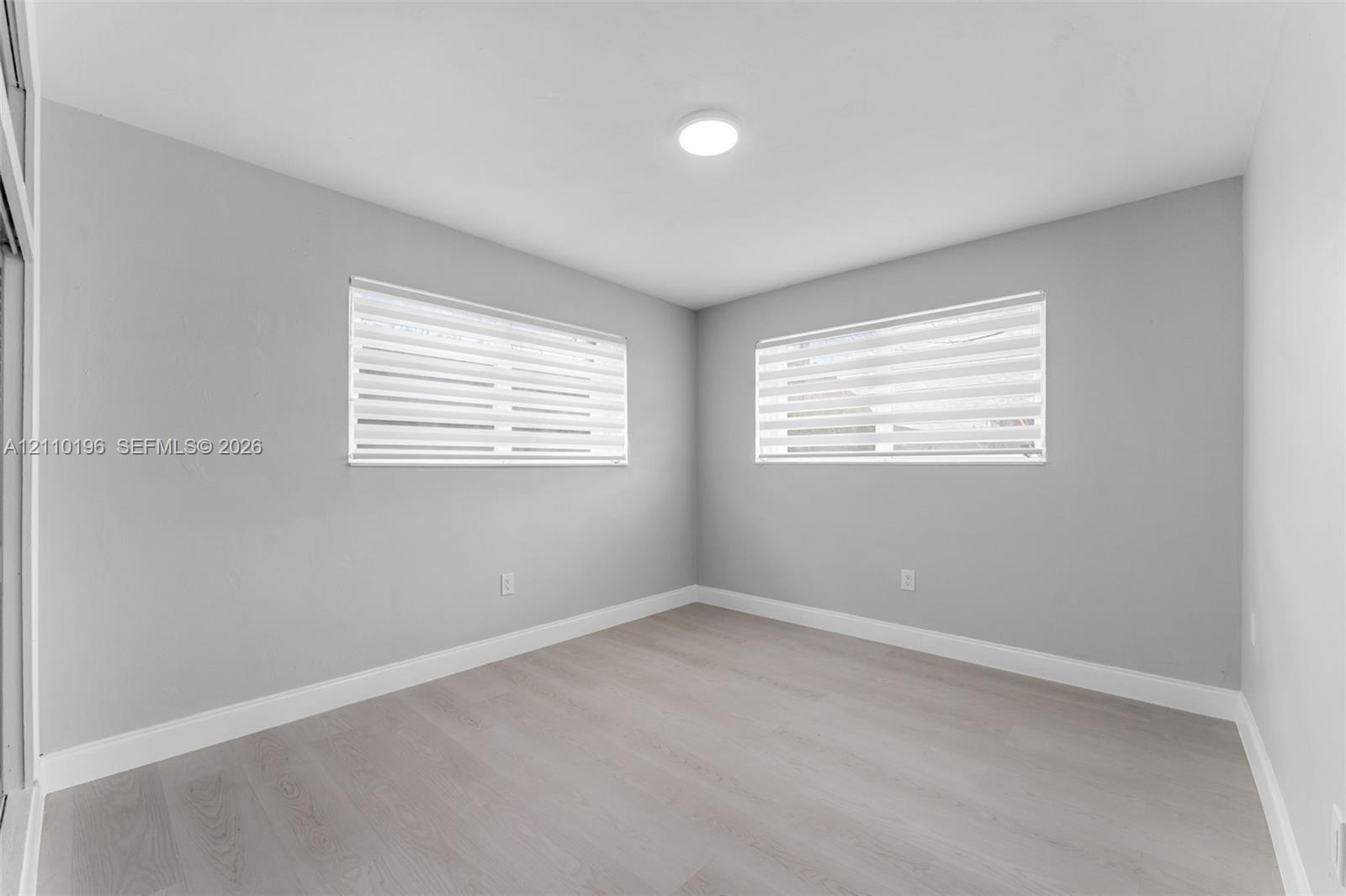 Neutral-toned interior featuring wood-finish flooring, light grey walls, recessed ceiling lighting, and windows equipped with dual-layered roller shades