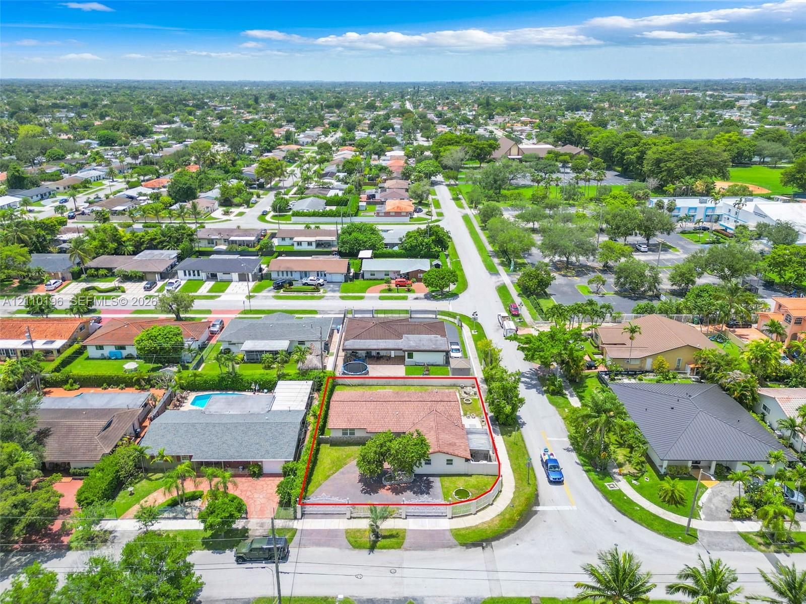Aerial perspective featuring a corner lot, paved driveway, sprawling lawn with mature landscaping, and a terracotta-tiled roof