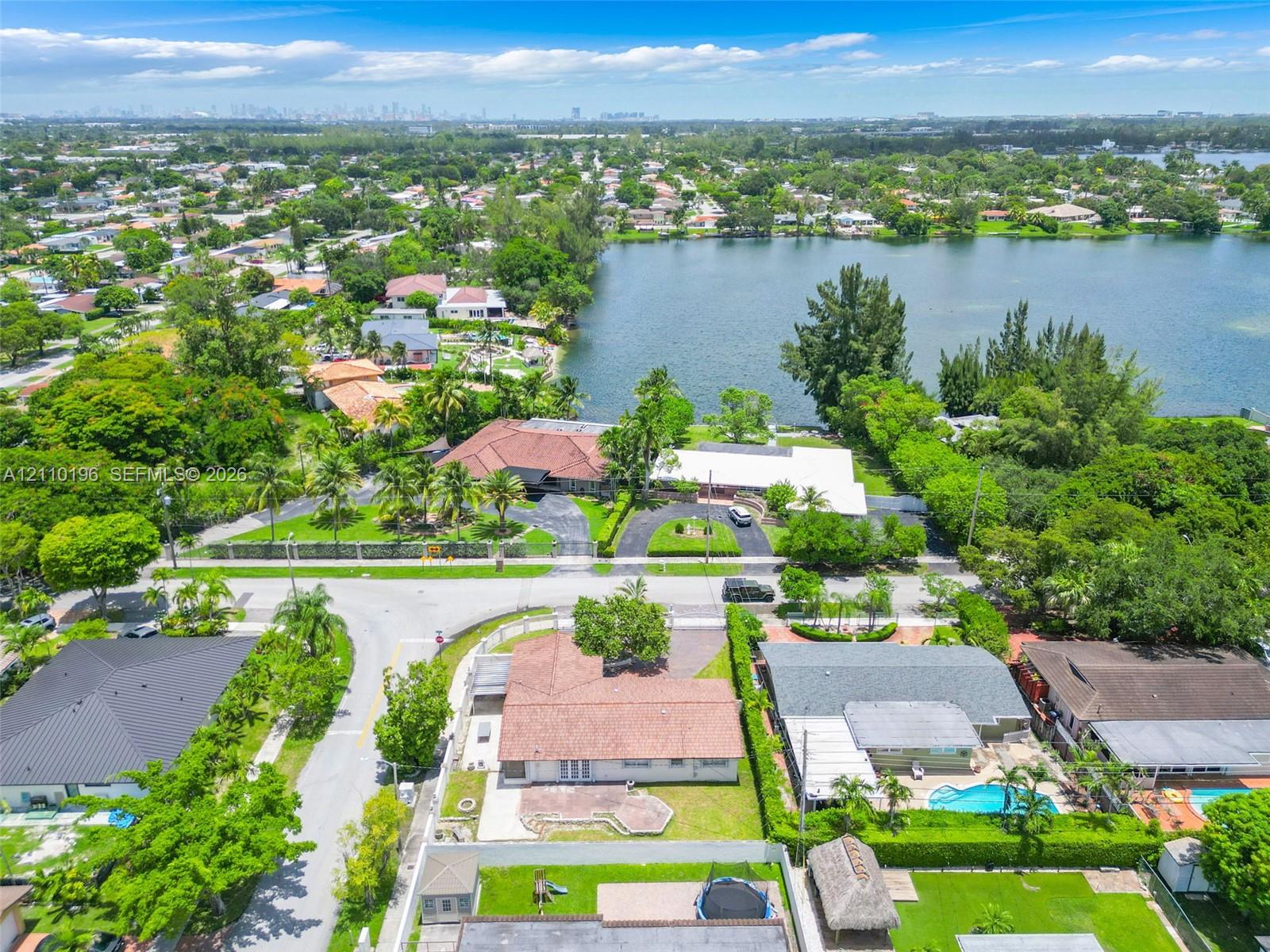 Aerial perspective of a multi-structure property featuring a sprawling tile roof, circular paved driveway, expansive waterfront acreage, and mature landscaping