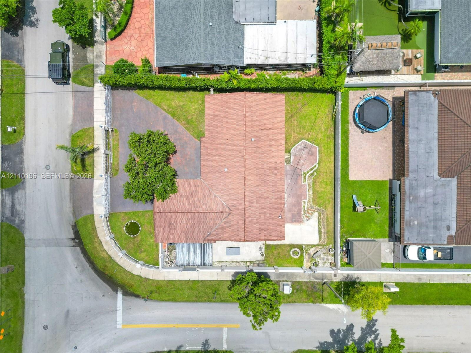 Aerial perspective of a corner lot property featuring a shingle roof, expansive green space, paved driveway, and perimeter fencing