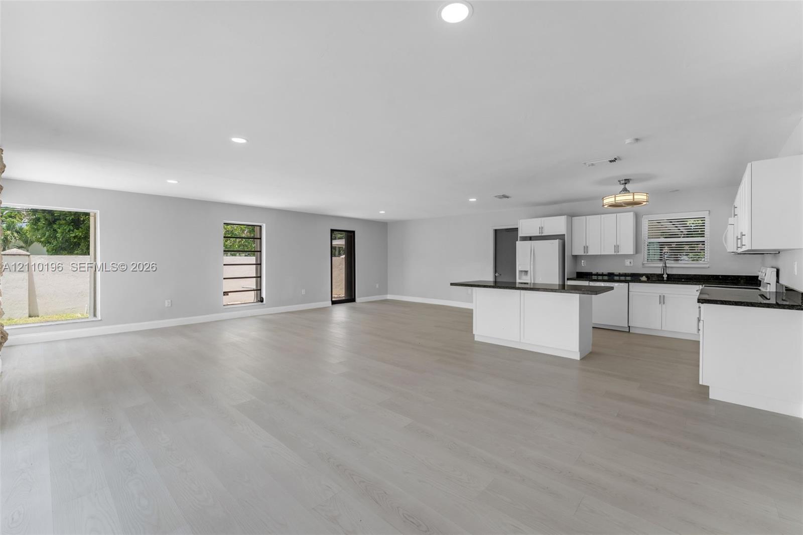 Open-concept kitchen featuring white shaker-style cabinetry, dark stone countertops, a center island, recessed lighting, and light-tone wood-finish flooring throughout
