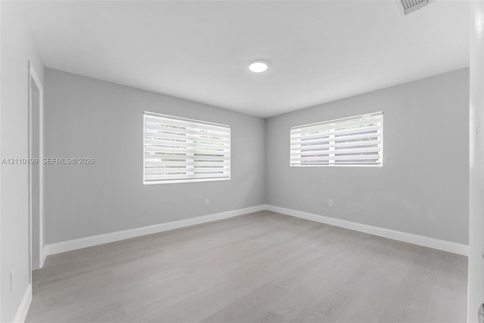 Neutral-toned interior space featuring wood-finish flooring, recessed lighting, and dual-pane windows with integrated light-filtering shades