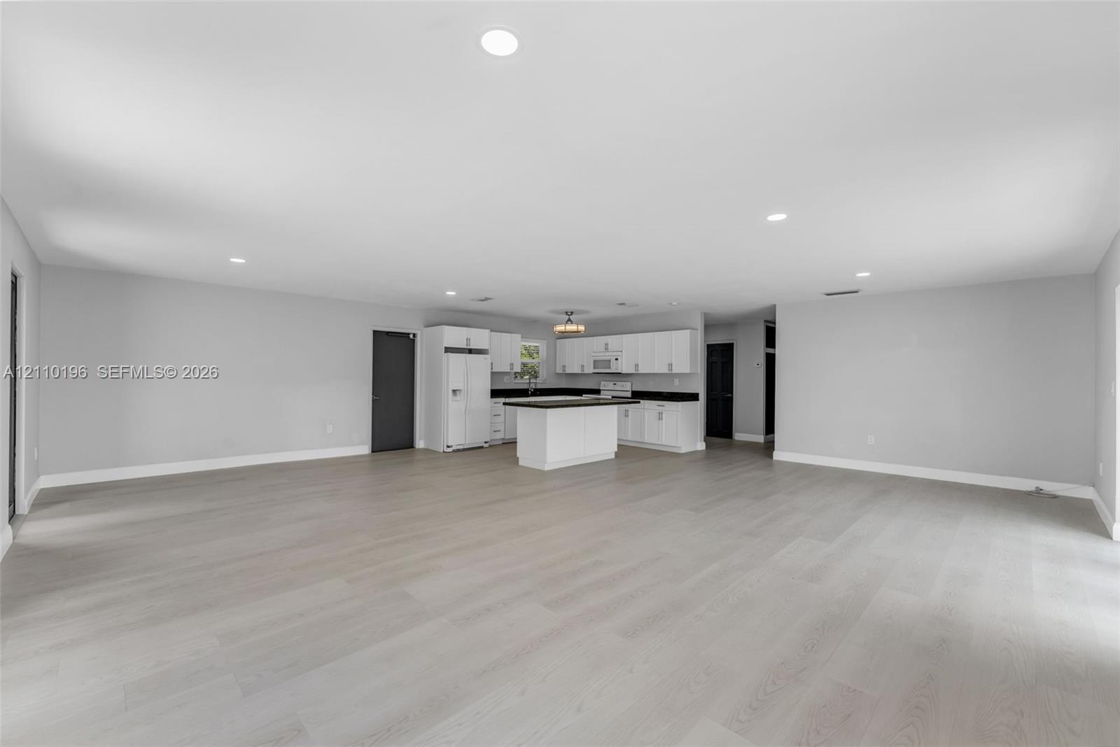 Open-concept interior featuring light wood-finish flooring, recessed lighting, and a kitchen equipped with white cabinetry, a center island, and dark-toned countertops