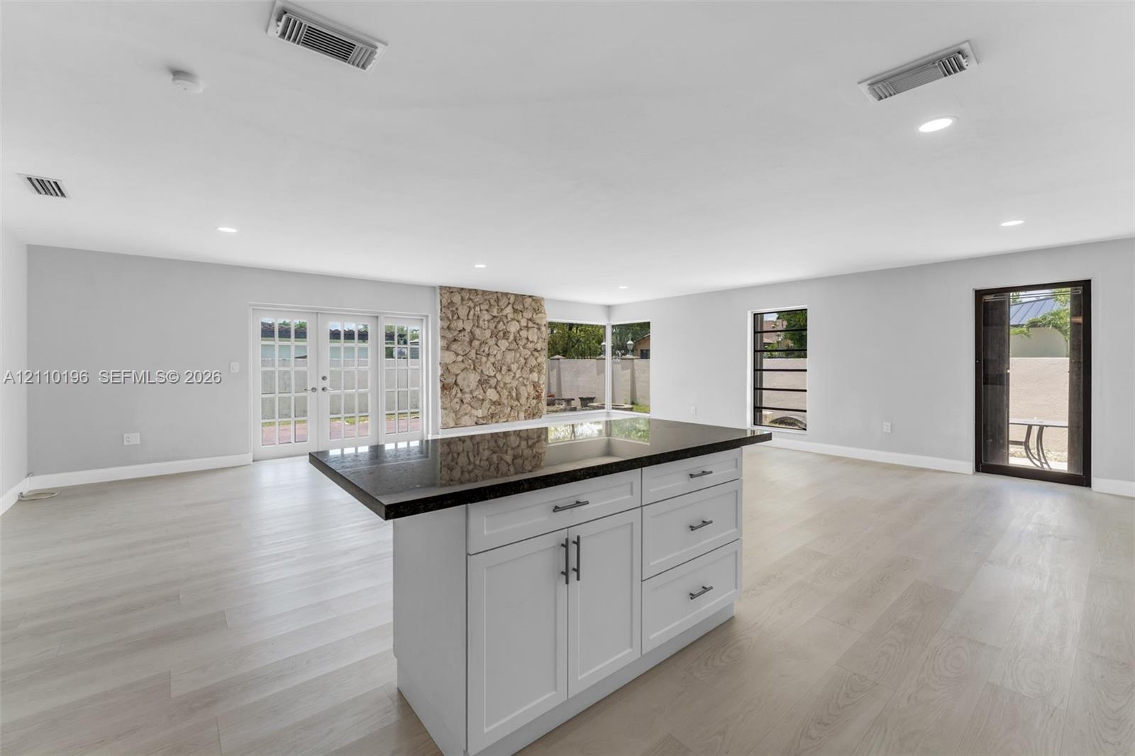 Center island featuring shaker-style cabinetry, dark stone countertop, and recessed lighting, accented by a floor-to-ceiling natural stone feature wall and wood-finish flooring