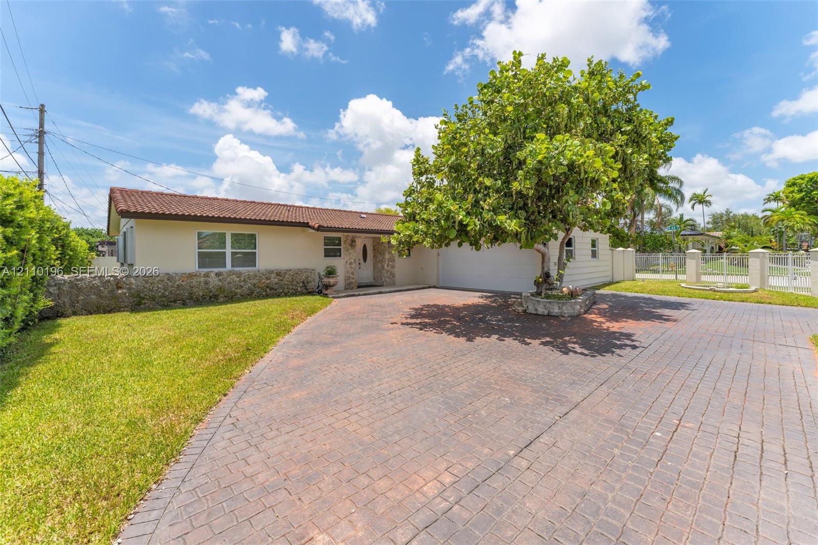 Single-story residence featuring a tile roof, natural stone exterior accents, a paved driveway, and a raised stone planter