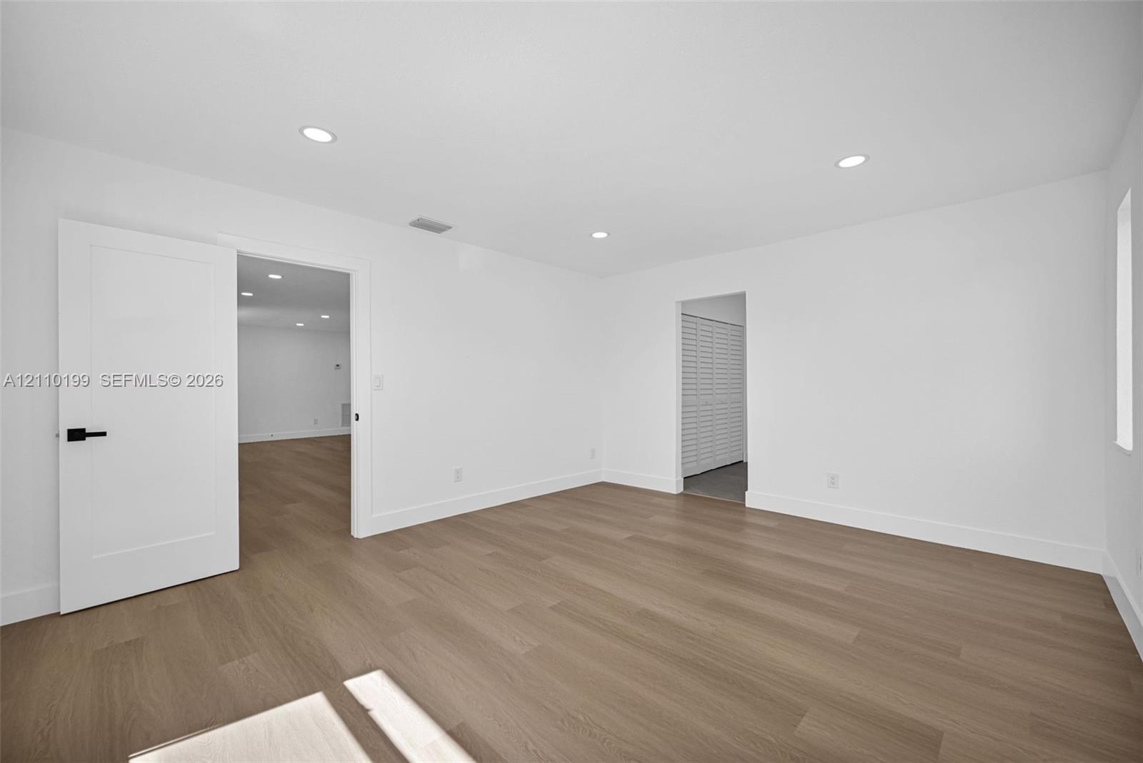 Interior space featuring wood-finish flooring, recessed lighting, and a white interior door with matte black hardware