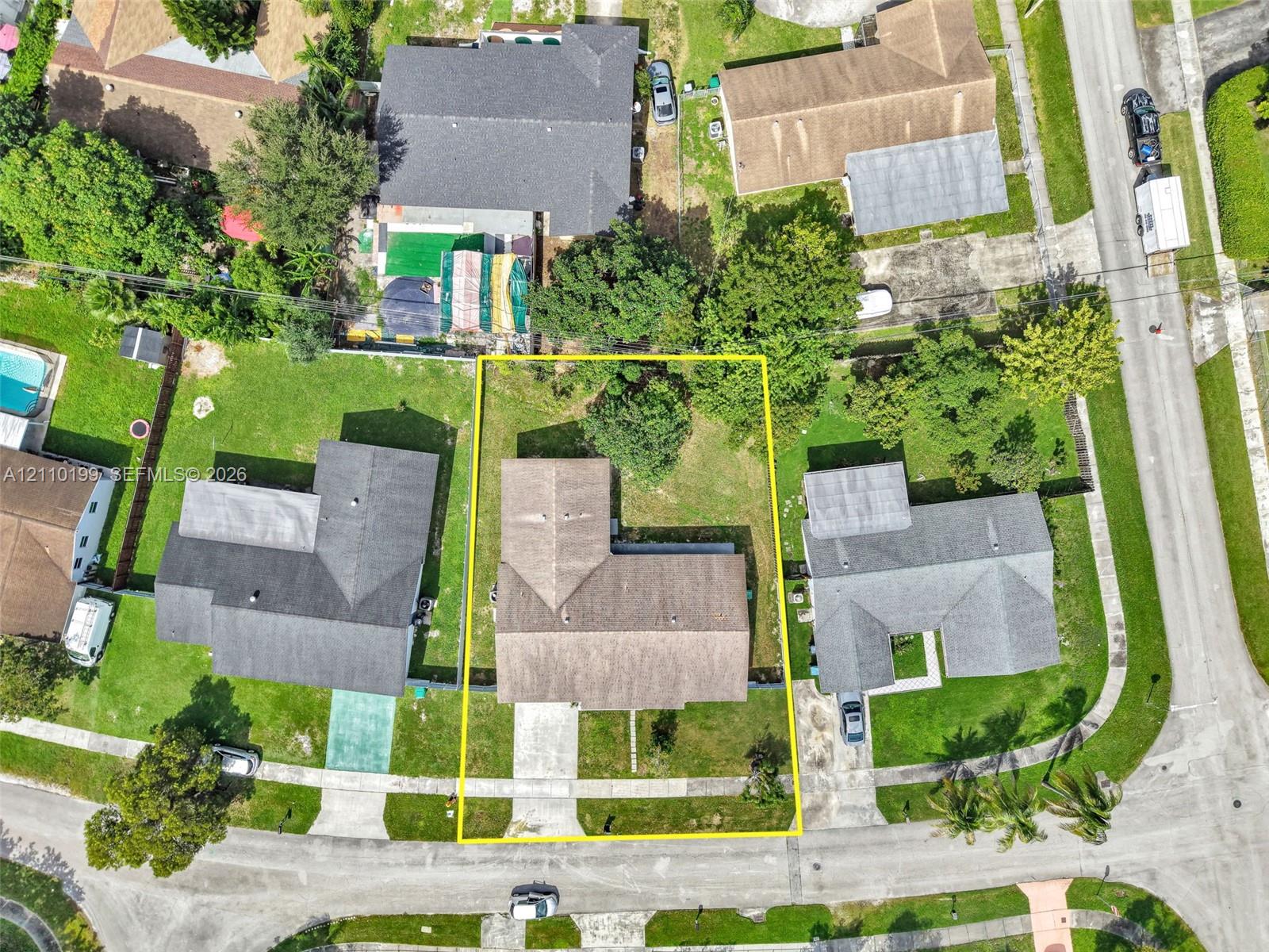Aerial view of residential property featuring a pitched-roof structure, concrete driveway, and established lawn with mature perimeter trees