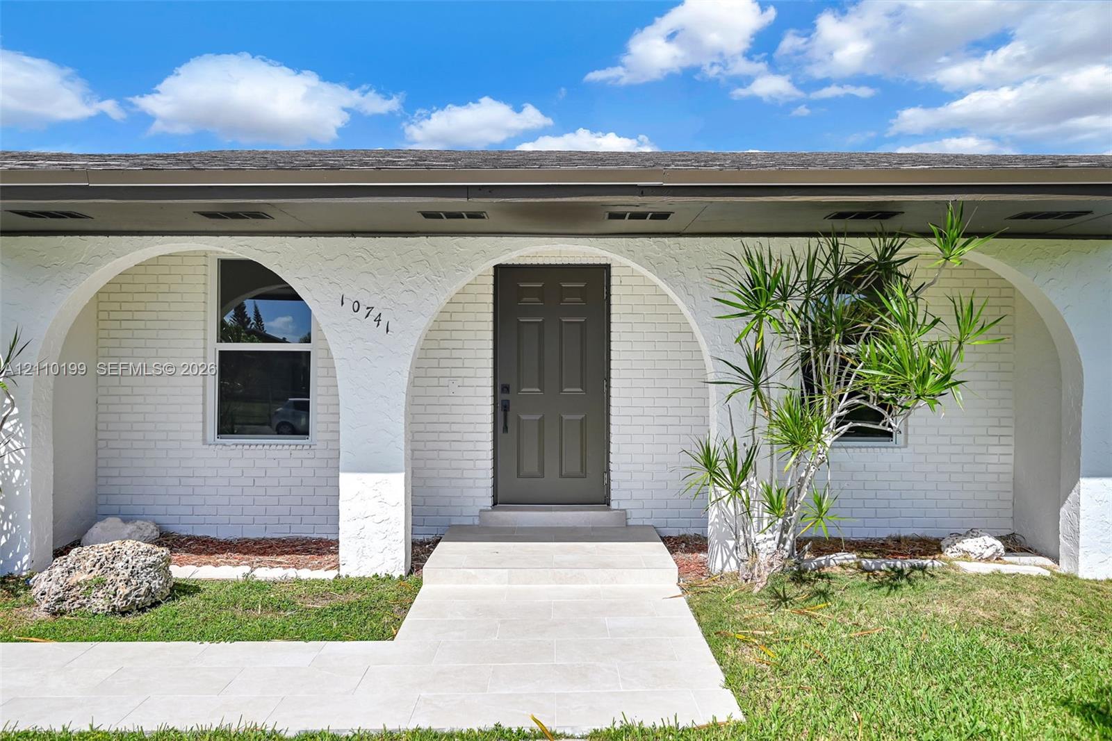 Exterior facade featuring white painted brick, arched entryways, a paneled front door, and a light-toned stone pathway