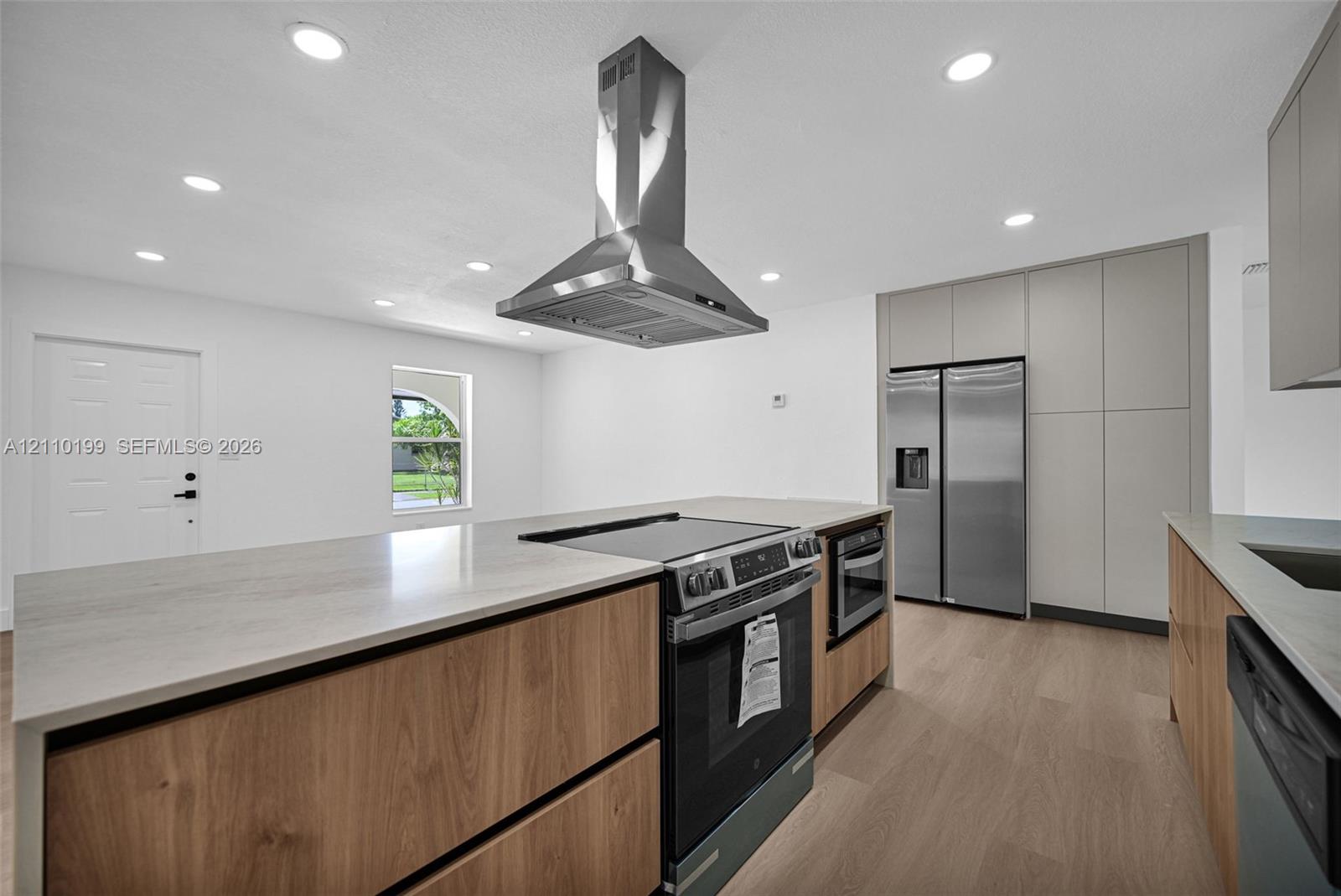 Kitchen featuring wood-finish cabinetry, a central island with a stone-composite countertop, a stainless steel range hood, built-in stainless steel appliances, and recessed lighting