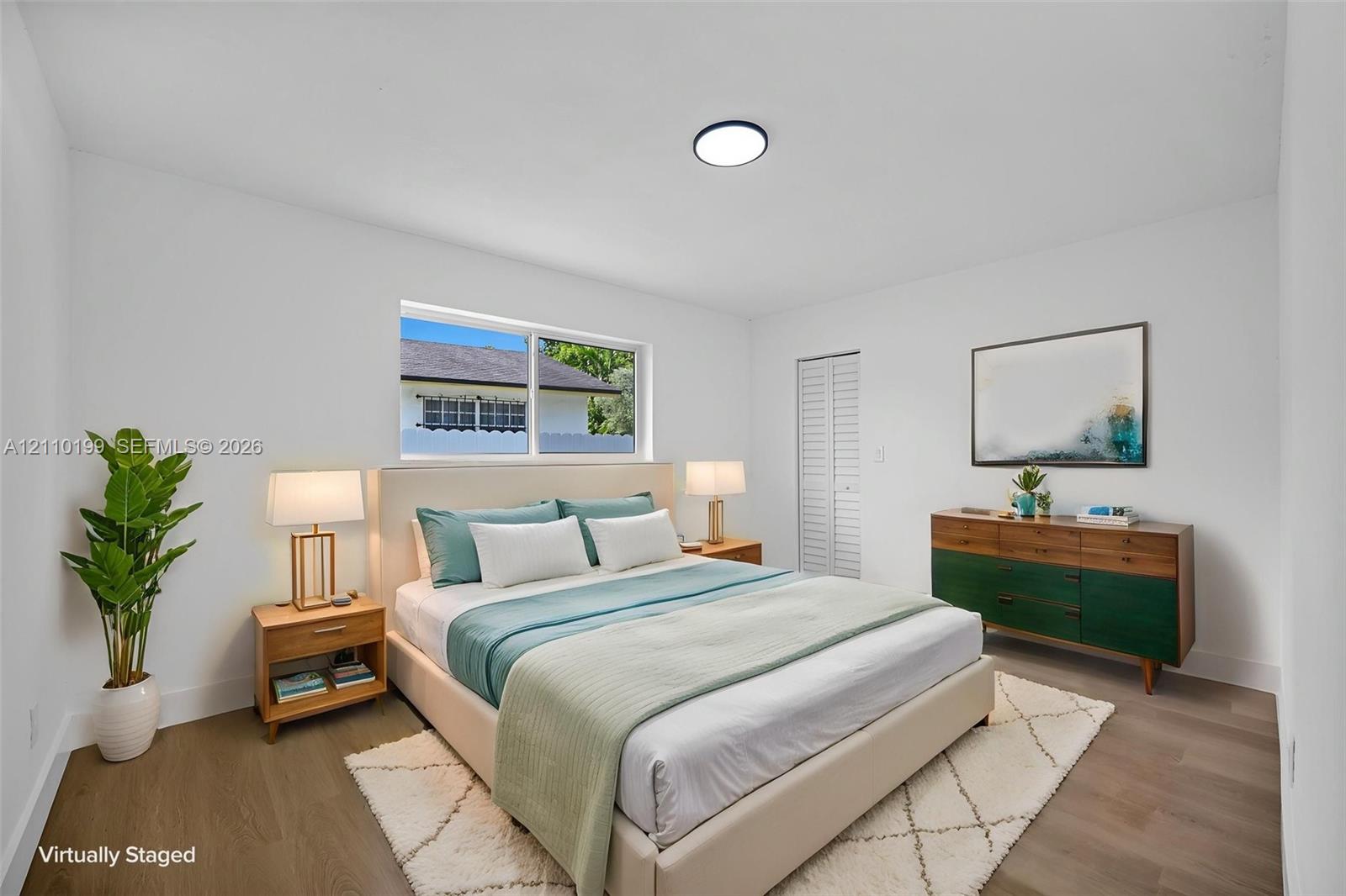 Room featuring wood-finish flooring, a horizontal sliding window, and a closet with bifold louvered doors, illuminated by a flush-mount ceiling fixture
