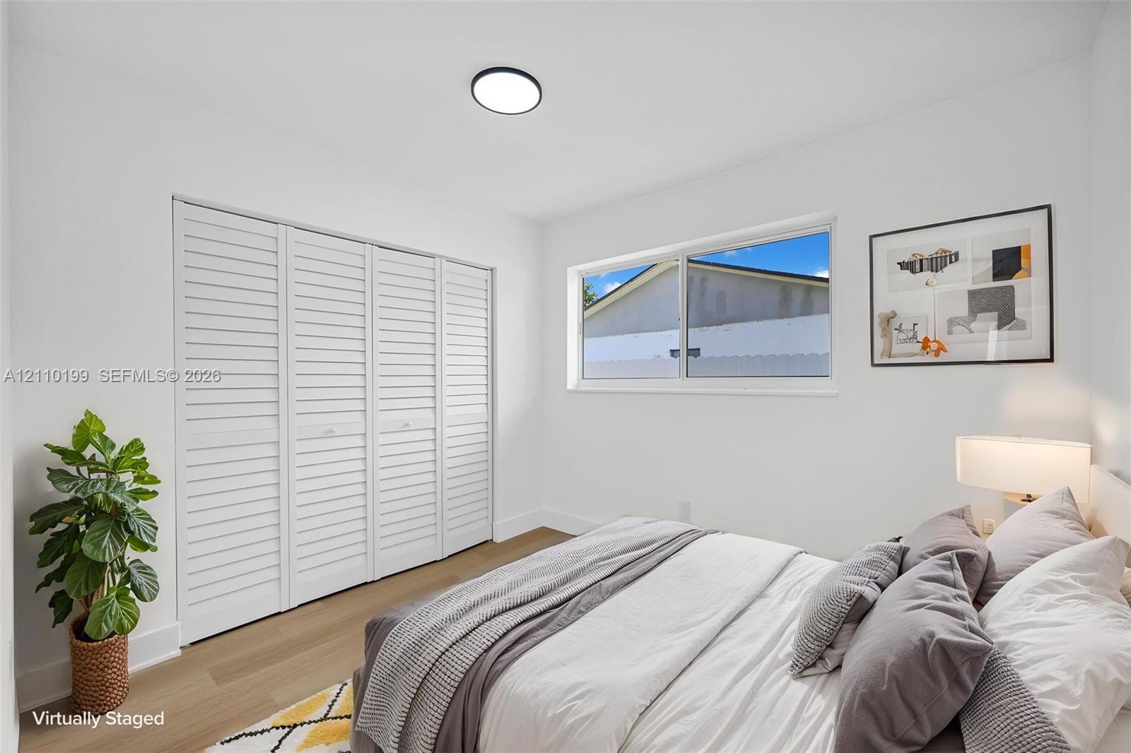 Room featuring wood-finish flooring, white walls, louvered closet doors, and a ceiling-mounted light fixture