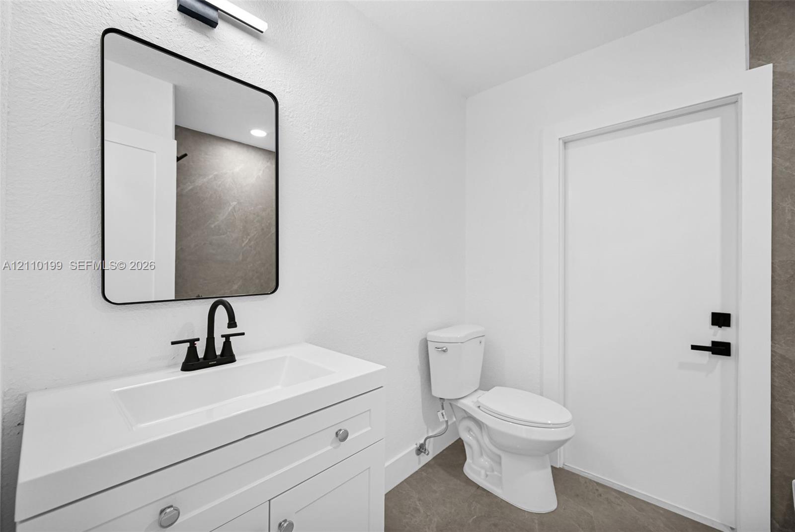 White vanity featuring an integrated rectangular sink and stone-surface countertop, matte black faucet, rectangular mirror with a black frame, and matte black door hardware