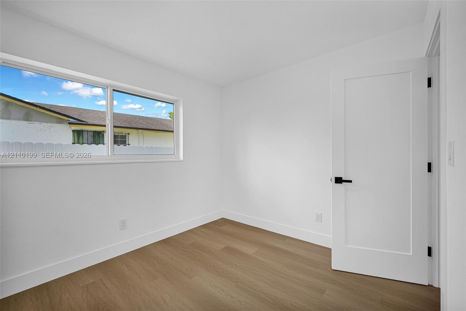 Room featuring wood-finish flooring, a horizontal sliding window, and a white interior door with matte black hardware