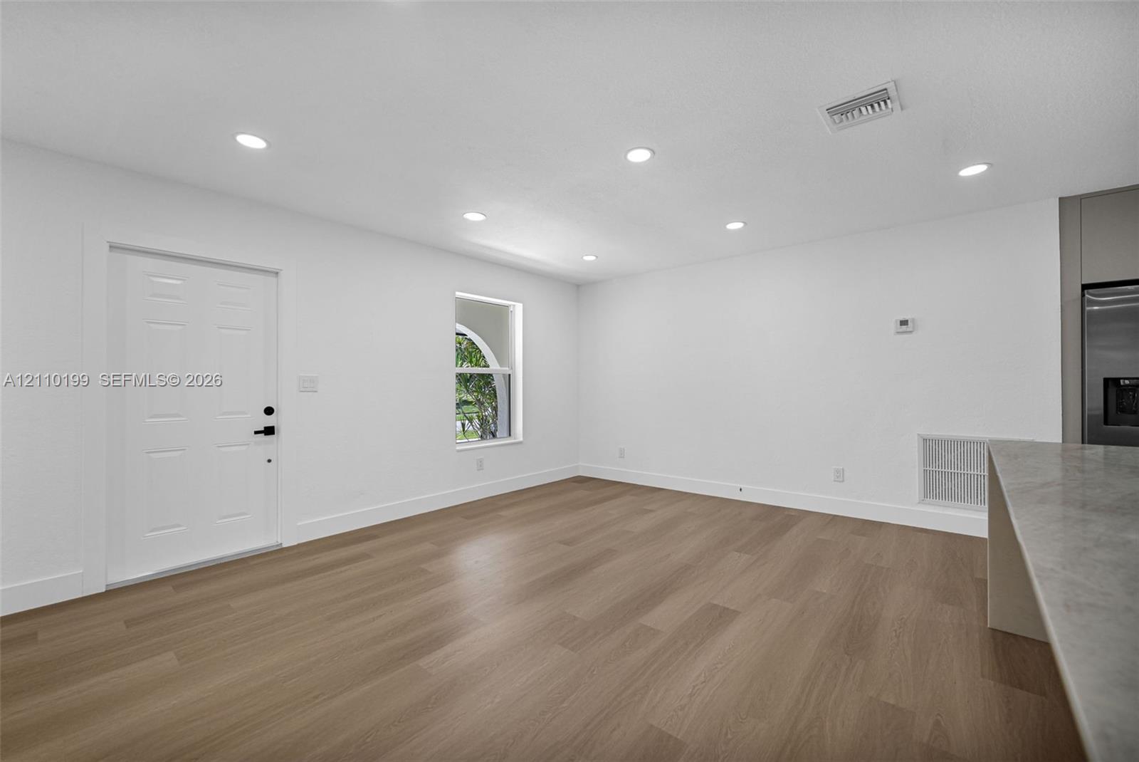 Wood-finish flooring, recessed lighting, arched window, and solid-core paneled entry door