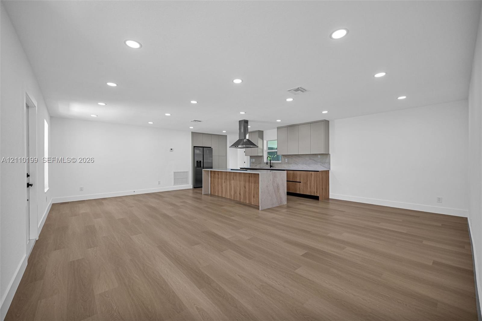 Open-concept space featuring wood-finish flooring, recessed lighting, a center island with a stone-finish waterfall edge, two-tone cabinetry, and a stainless steel vent hood