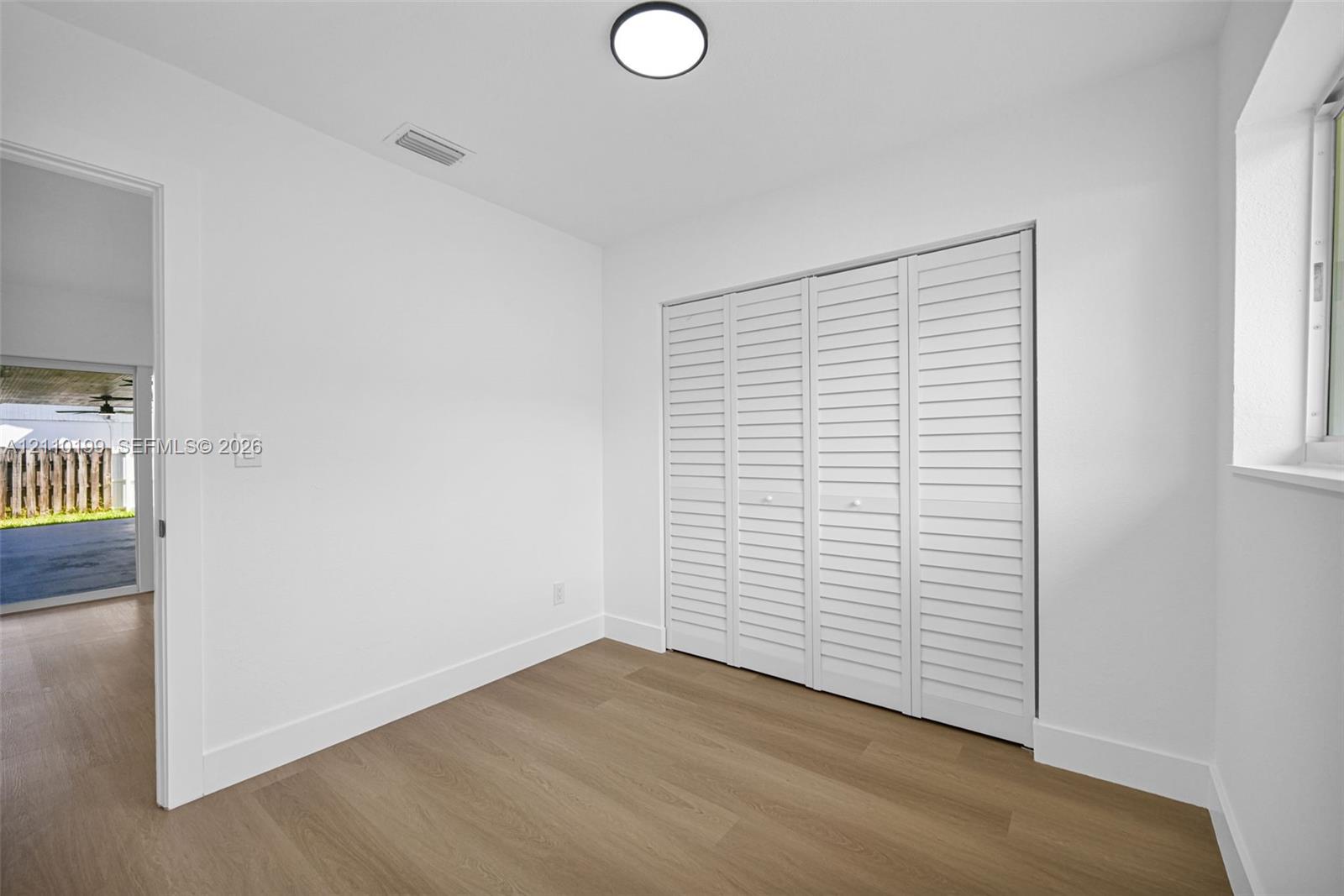 Neutral interior featuring wood-finish flooring, white louvered closet doors, and a ceiling-mounted LED light fixture