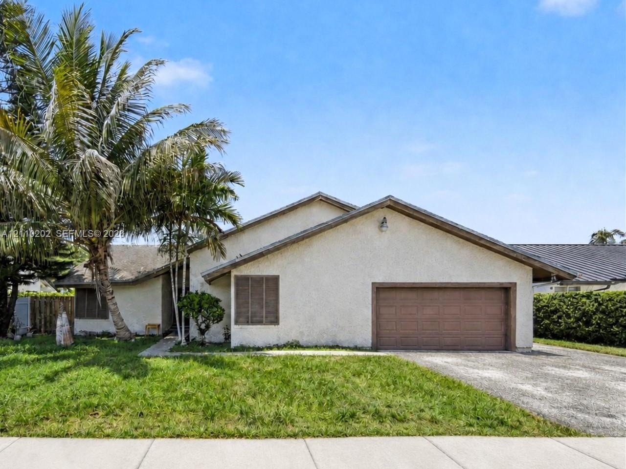Single-story stucco exterior with a gabled roofline, attached multi-car garage, mature palm trees, and front yard landscaping