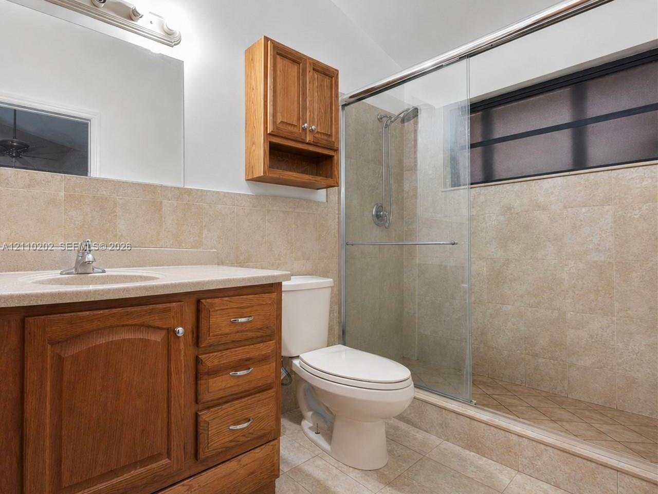 Bathroom featuring wood-finish cabinetry, a neutral-toned countertop with an integrated sink, tiled wall surrounds, and a glass-enclosed walk-in shower