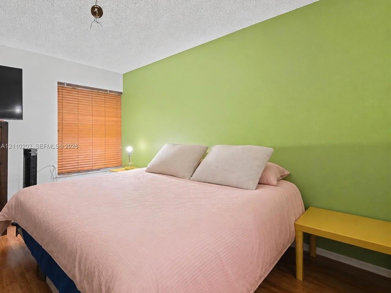 Room featuring wood-finish flooring, a textured ceiling, and a window fitted with horizontal blinds