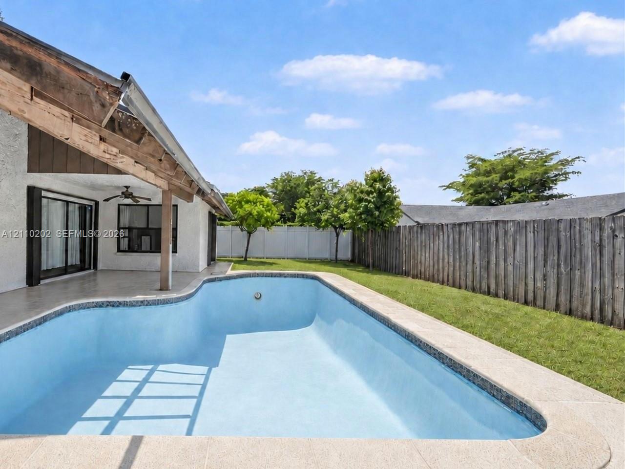 Backyard featuring an in-ground swimming pool, concrete patio, covered porch with exposed wood beams, and perimeter wood fencing