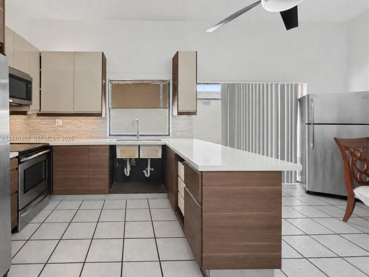 Kitchen featuring two-tone flat-panel cabinetry, light-toned quartz countertops, dual-basin farmhouse sink, stainless steel appliances, and tile flooring