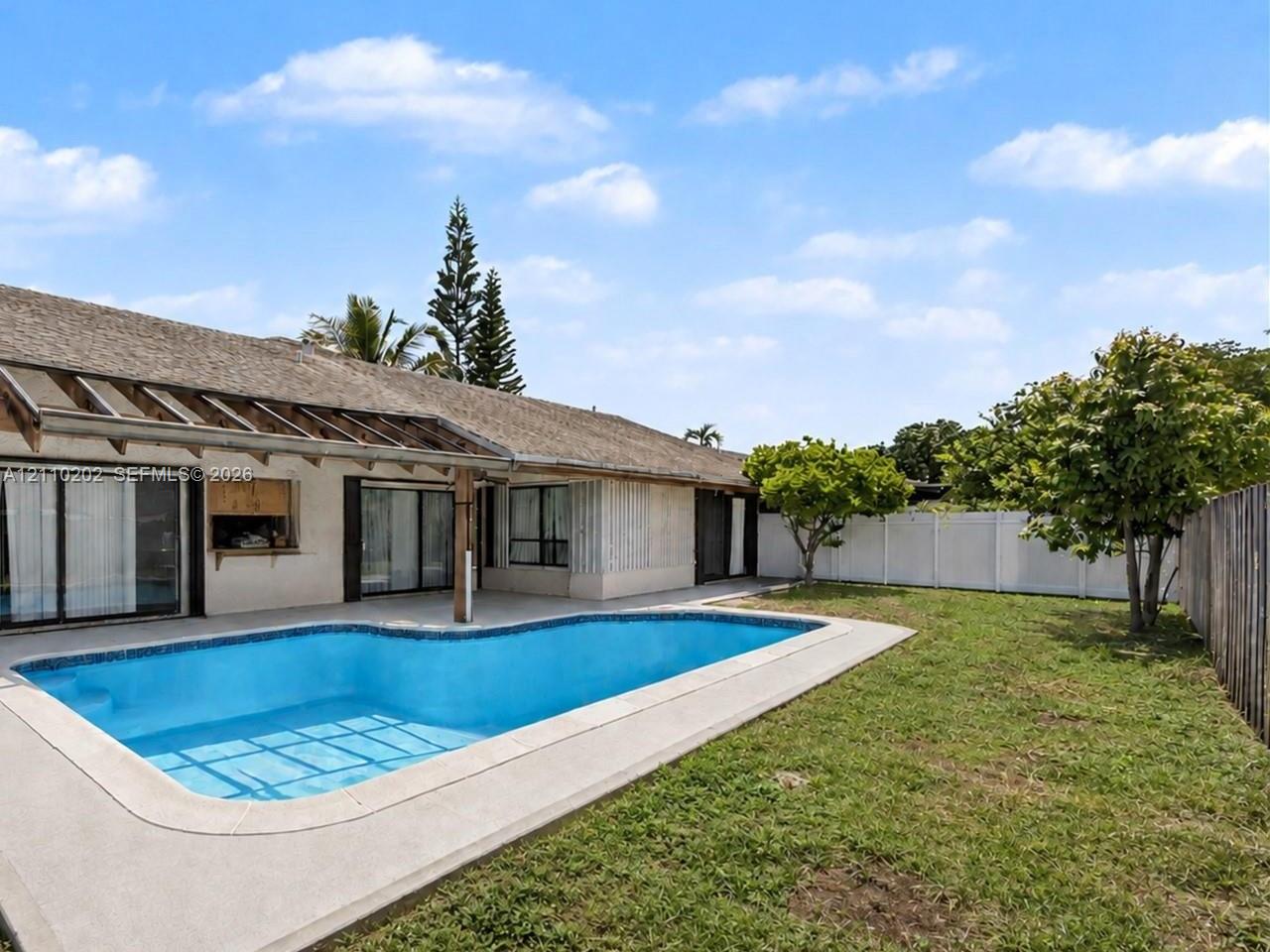 In-ground swimming pool with concrete decking, covered outdoor patio, and perimeter privacy fencing