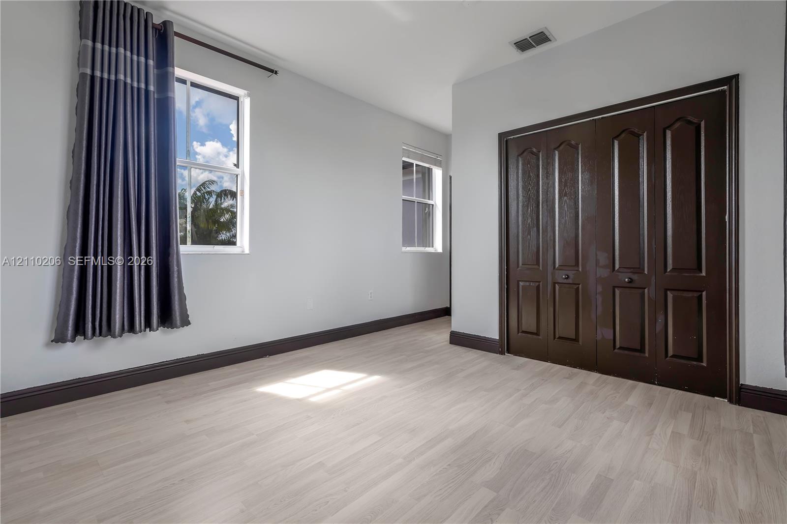 Light-toned wood-finish flooring, dual windows providing natural light, and dark-finished wood bifold closet doors