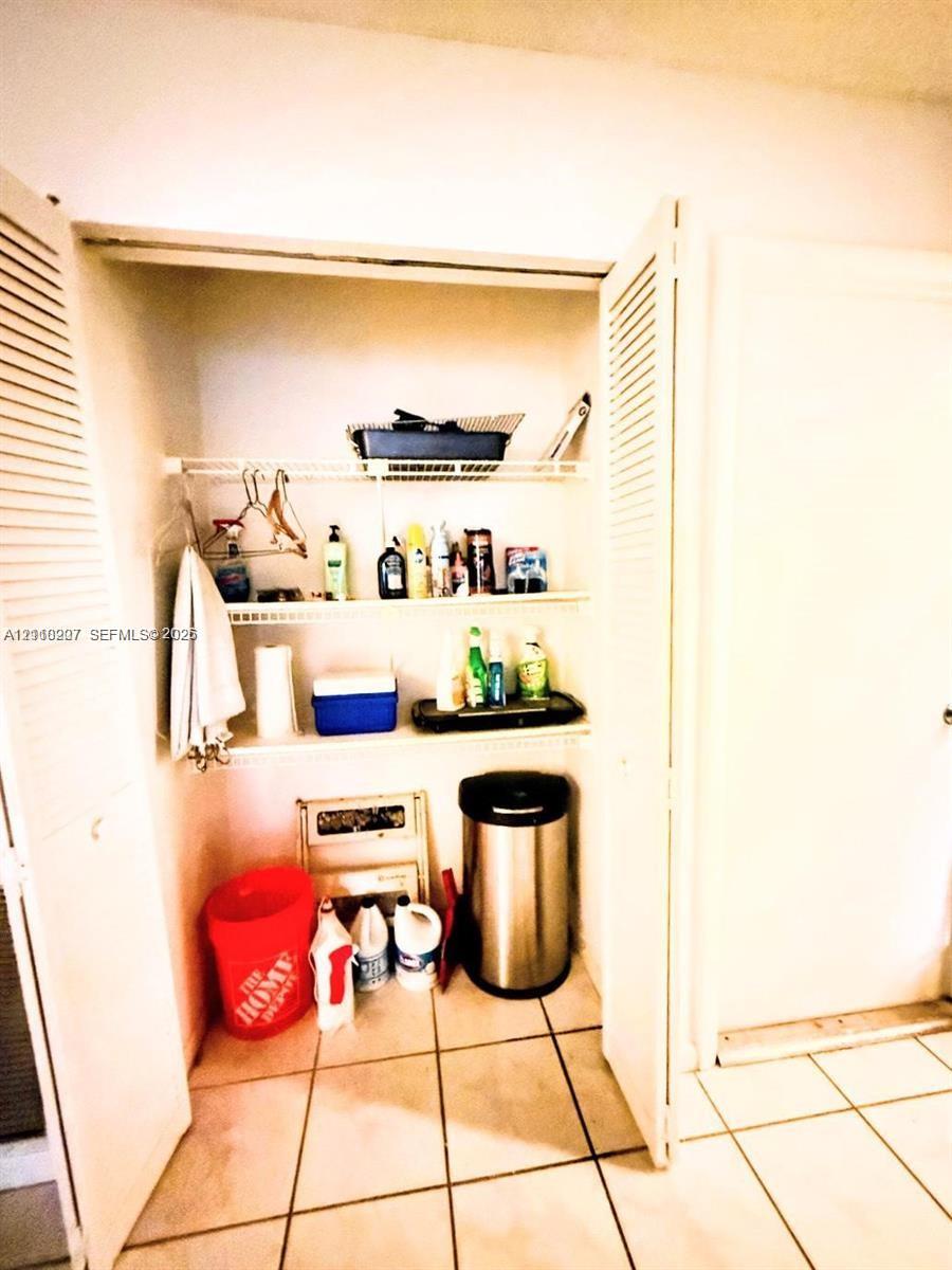 Storage closet featuring dual louvered doors and three tiers of built-in wire shelving, finished with tile flooring