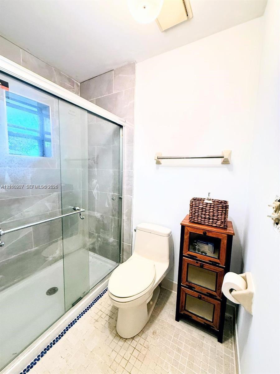 Walk-in shower with floor-to-ceiling tile surround and sliding glass doors, integrated toilet, and tiled flooring