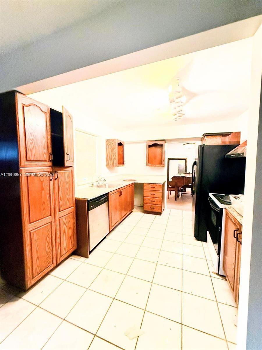 Kitchen featuring wood cabinetry, integrated dishwasher, solid surface countertops, ceramic tile flooring, and black appliances