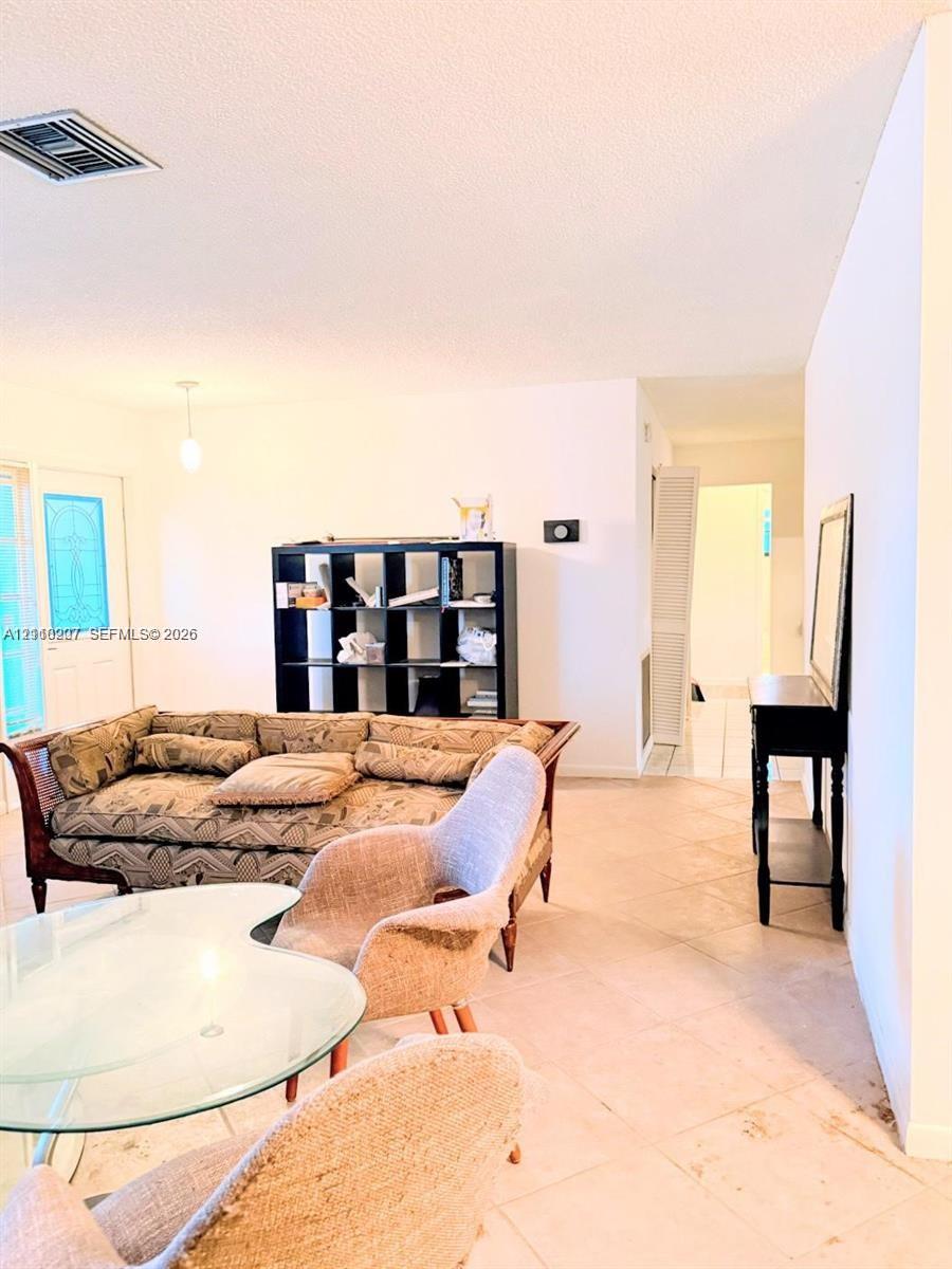 Open-concept interior featuring light-toned tile flooring, neutral wall finishes, and a decorative glass-panel entry door
